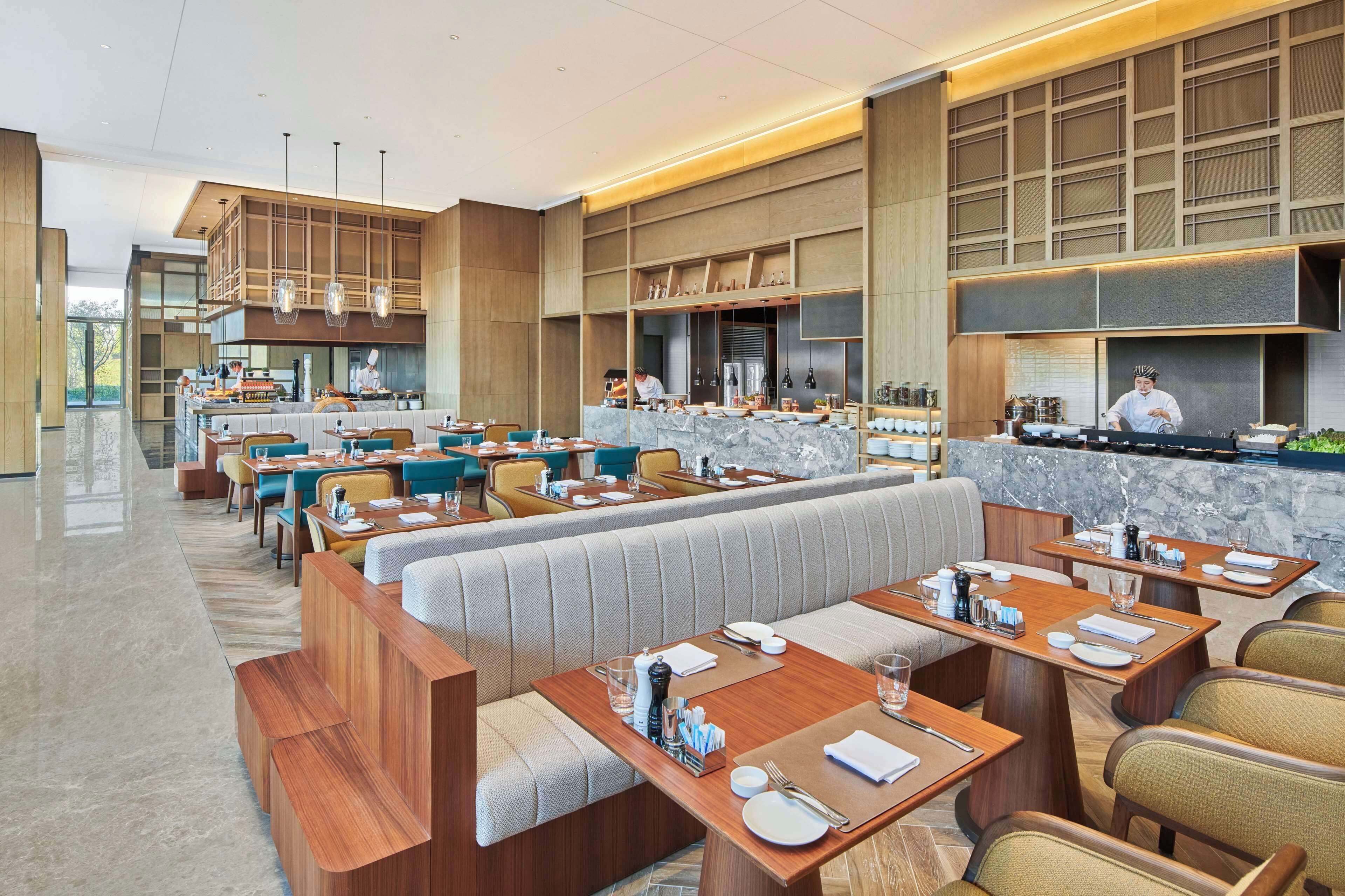 A modern restaurant with a central bar area, multiple dining booths, and a chef preparing food.