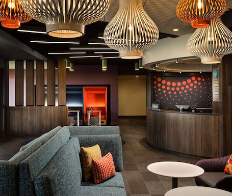 A modern hotel lobby with a reception desk, seating area, and unique lighting fixtures.