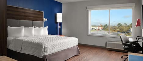 A hotel room with a large bed, a desk, a chair, a window with a view of the outside, and a lamp.