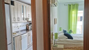 Eine moderne Küche mit Holzschränken und einem Geschirrspüler, ein Schlafzimmer mit einem Bett, einem Nachttisch und einem grünen Vorhang.