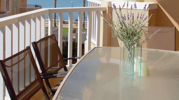 Ein Balkon mit Glastisch, Stühlen und einem Blumenstrauß.