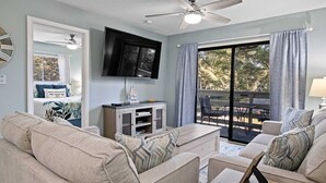 A living room with a ceiling fan, a flat-screen TV, a sofa, a coffee table, and a view of an outdoor patio.