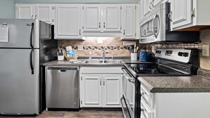A modern kitchen with white cabinets, stainless steel appliances, a granite countertop, and a tiled backsplash.