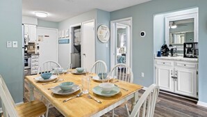 A dining room with a wooden table set for four, white chairs, and a ceiling fan.