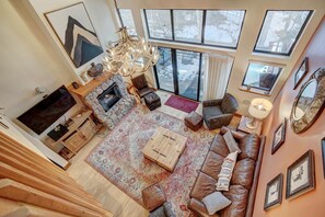 A spacious living room with a stone fireplace, leather sofa, and a large window offering a view of the outdoors. - Walk To Town, Free Shuttle To Ski, Peak 9 Location, Fireplace, Hot Tub, Value (Breckenridge)