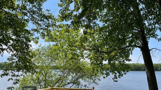 A lakeside deck with outdoor seating and a dock extending into the water. - Lake home, across the street from a golf course & minutes to shopping and more! (Sauk Centre)