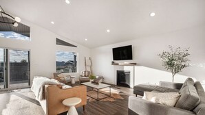 Uma sala de estar espaçosa com lareira, janelas amplas e uma televisão de tela plana.
