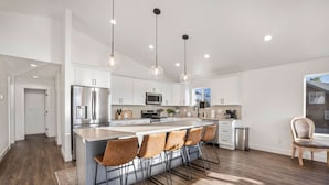 Uma cozinha moderna com uma ilha central, banquetas, eletrodomésticos de aço inoxidável e iluminação pendente.