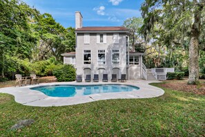 A two-story house with a swimming pool, surrounded by lush greenery and trees.