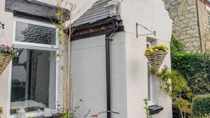 Un bâtiment blanc avec un mur en pierre, une fenêtre à cadre noir et deux jardinières suspendues.