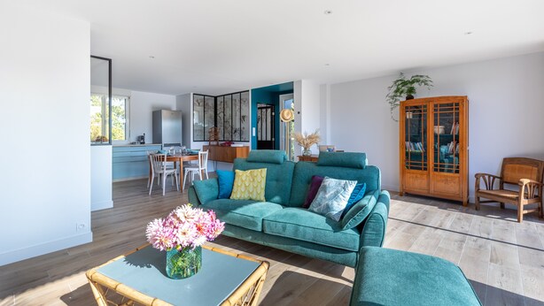 Un salon spacieux avec un canapé de couleur turquoise, une table basse et un coin repas à l’arrière-plan.
