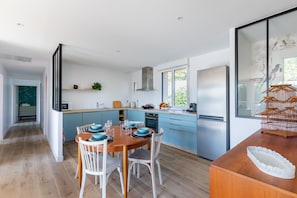 Une cuisine moderne avec des meubles de couleur bleue, une table à manger en bois et des chaises blanches.