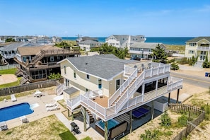 A multi-story house with a pool, outdoor seating, and a view of the beach.