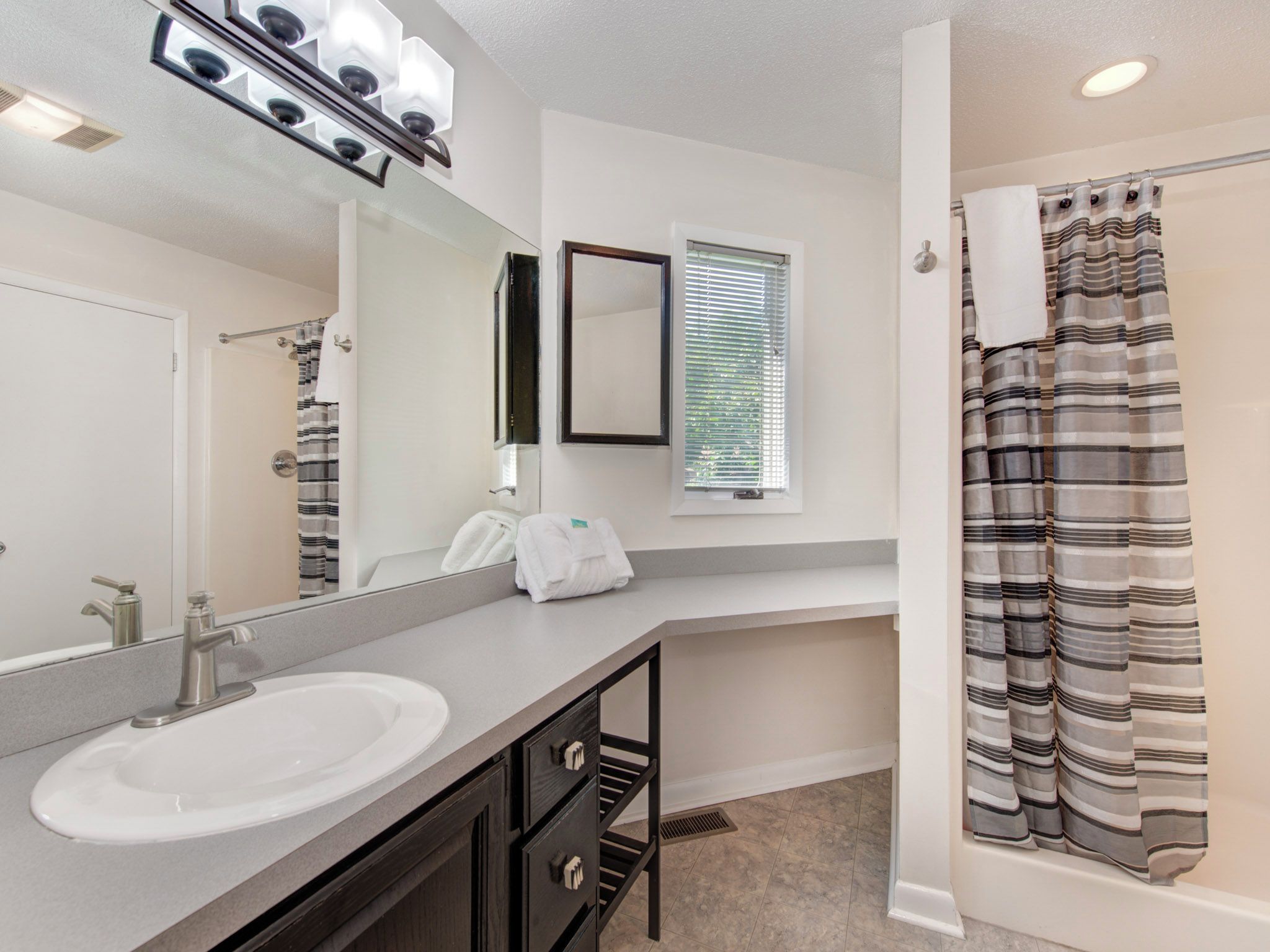 A bathroom with a large mirror, a sink, a towel rack, and a shower curtain.