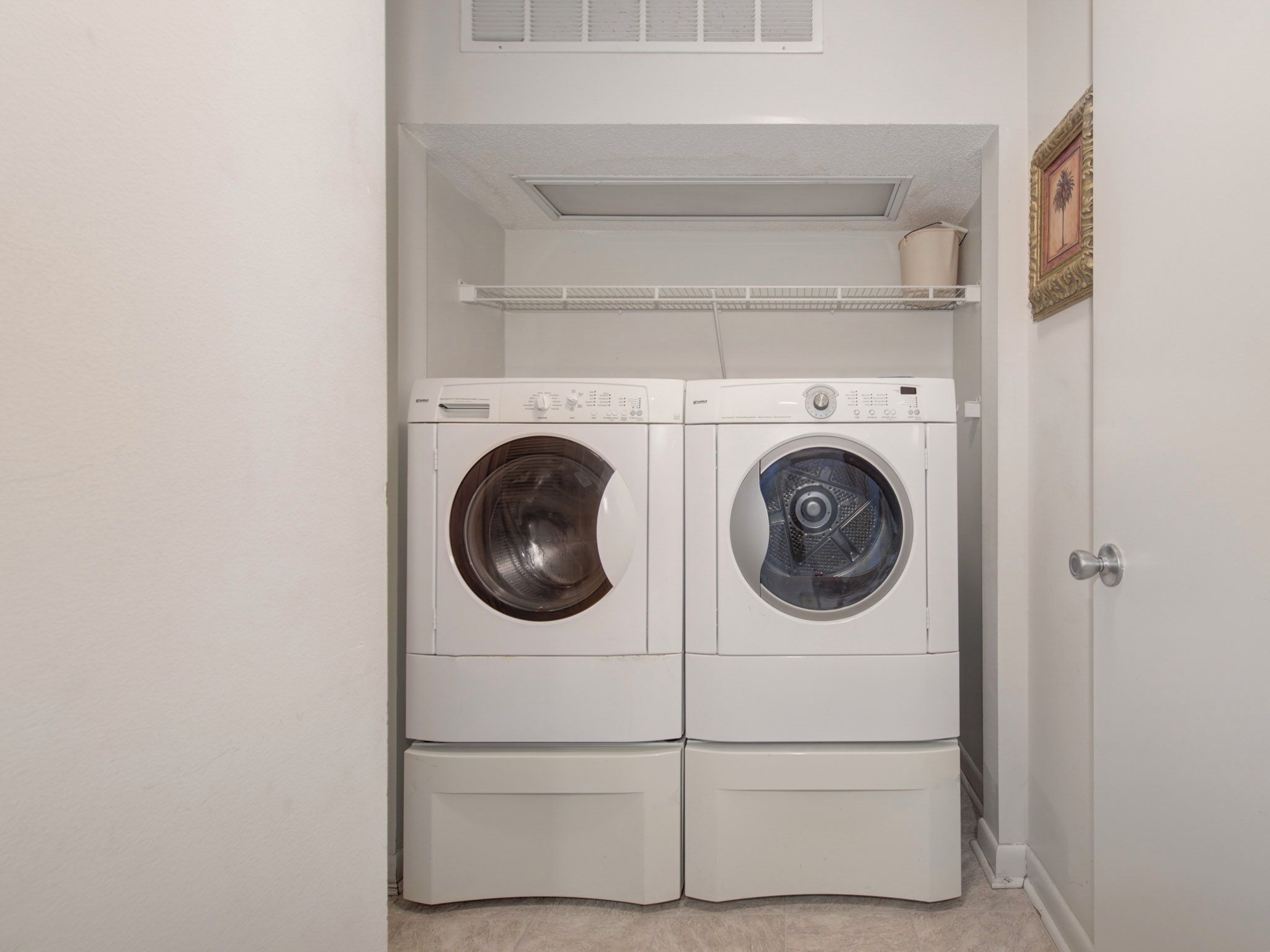 A laundry room with two stacked front-loading washing machines and a shelf above them.