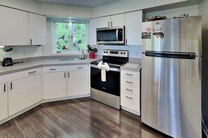 A modern kitchen with white cabinets, stainless steel appliances, and a window with a view of greenery. - Birdsong by Jackson Mountain Rentals (Gatlinburg)