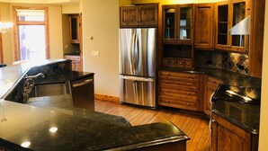 Una cocina con armarios de madera, un refrigerador de acero inoxidable, una cubierta de encimera negra y un ventilador de techo.