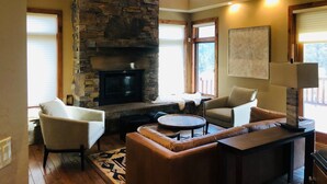 Un salón amplio con chimenea de piedra, asientos cómodos y ventanas grandes.