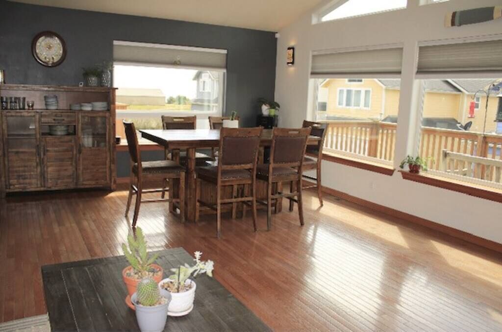 A dining area with a wooden table and chairs, a potted plant, and a view of a balcony with a railing.