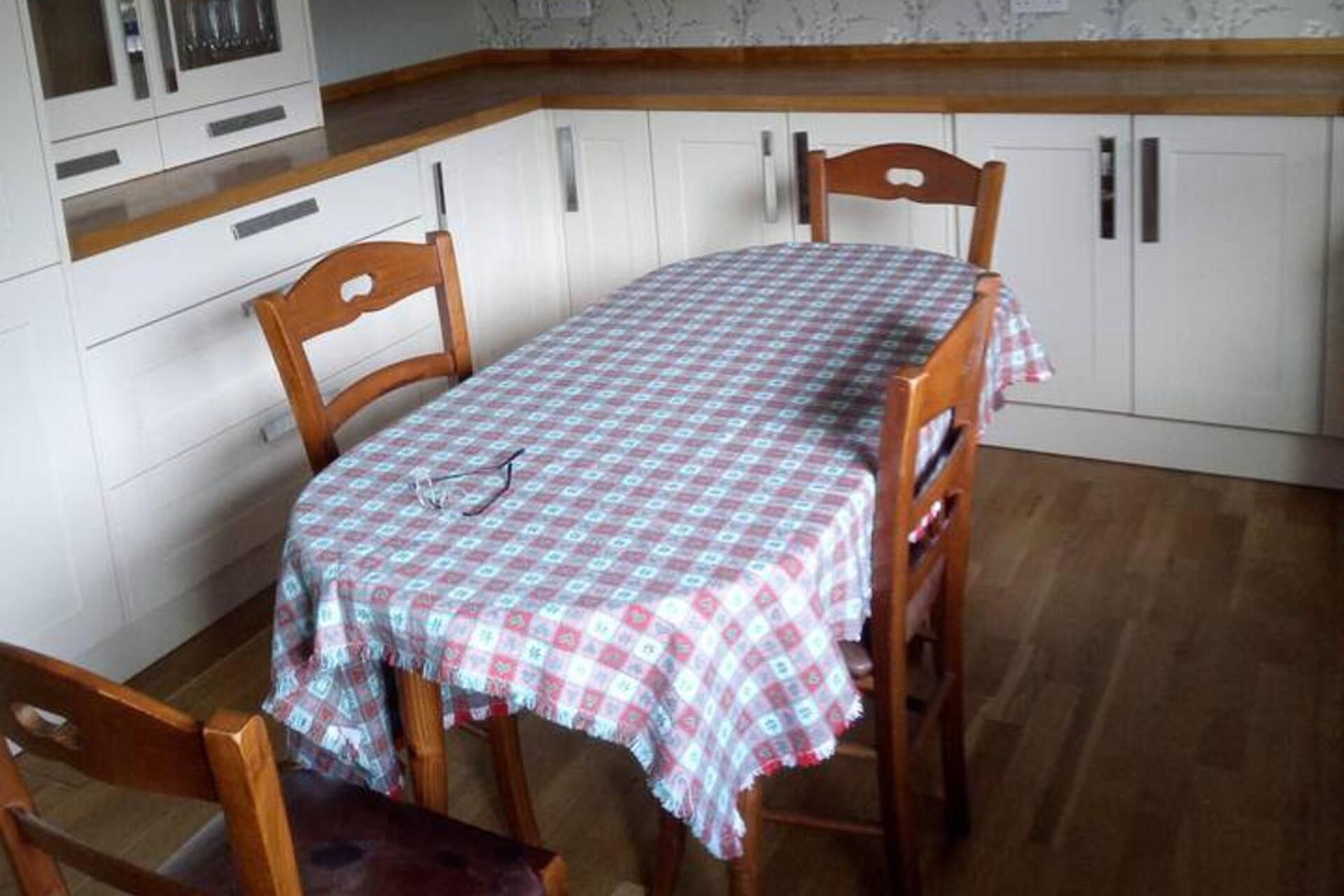 Un coin repas avec une table recouverte d’une nappe à carreaux, des chaises en bois et des meubles blancs.