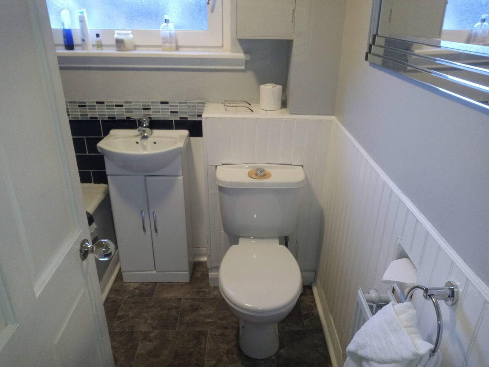 A small bathroom with a white sink, toilet, and a window above the sink.