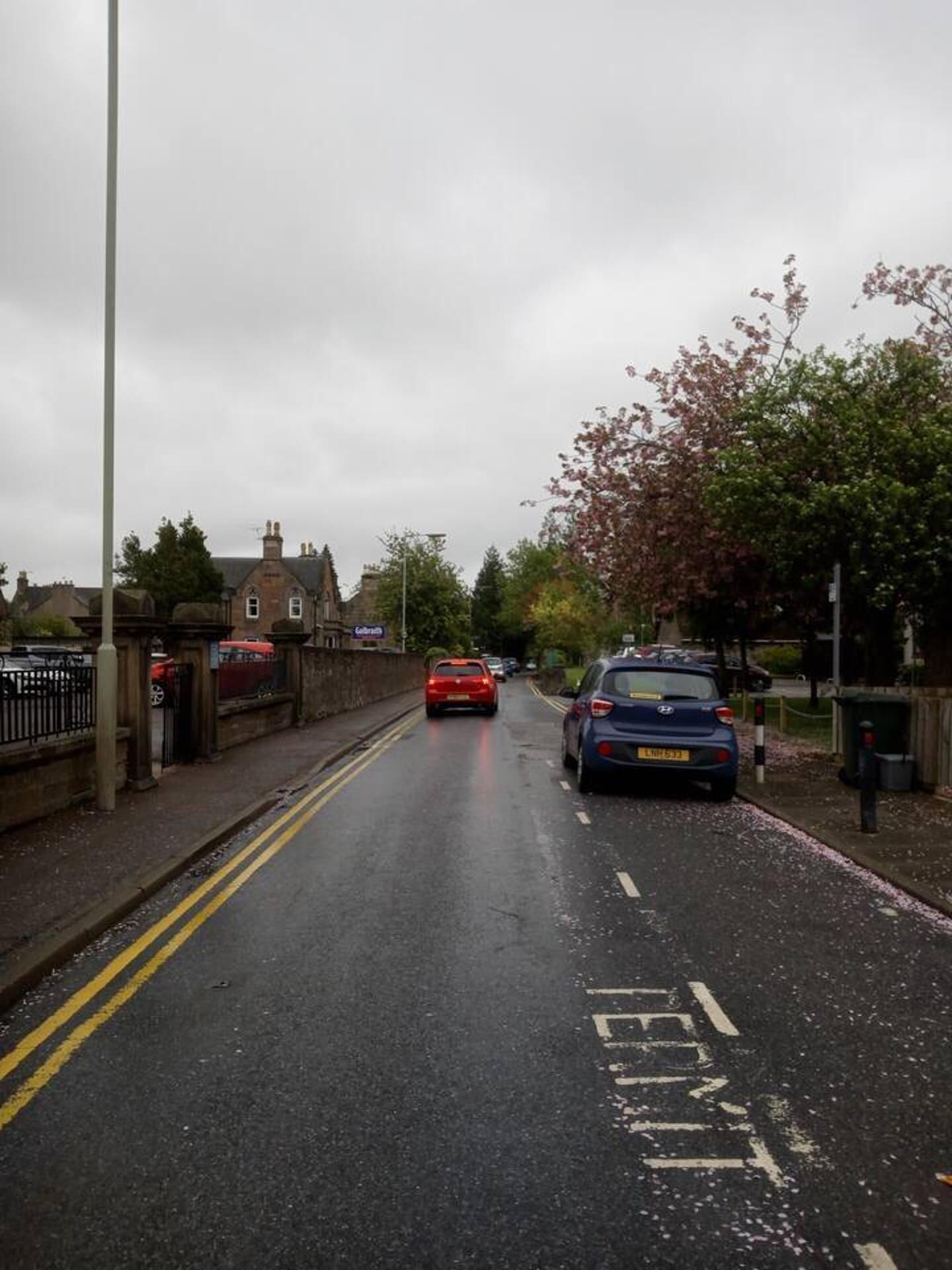 Calle con coches aparcados al lado, una vía despejada y un edificio con un cartel que dice 'Coleshill'.