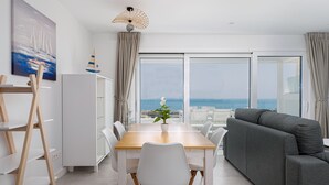 A modern living room with a dining area, large windows, and a view of the sea.