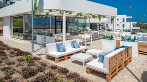 An outdoor seating area with white furniture, a glass enclosure, and a view of the sea.