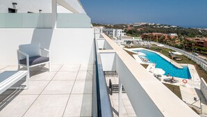 A rooftop pool area with a clear view of the sea, a chair, and a poolside lounge.
