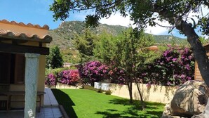 Ein gepflegter Garten mit Terrasse, Steinmauer und blühenden Bäumen.