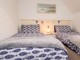 Una cama doble con ropa de cama a juego de diseño de peces, una mesita de noche con una lámpara y un cuadro en la pared.