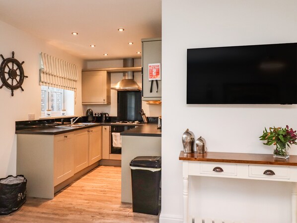 A modern kitchen with a central island, a stove, and a sink. There is a television mounted on the wall and a small table with decorative items.