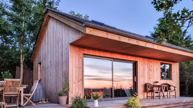 A wooden cabin with a patio, outdoor seating, and a large sliding glass door.