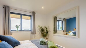 A bedroom with a bed, a large mirror, a window with curtains, and a potted plant.