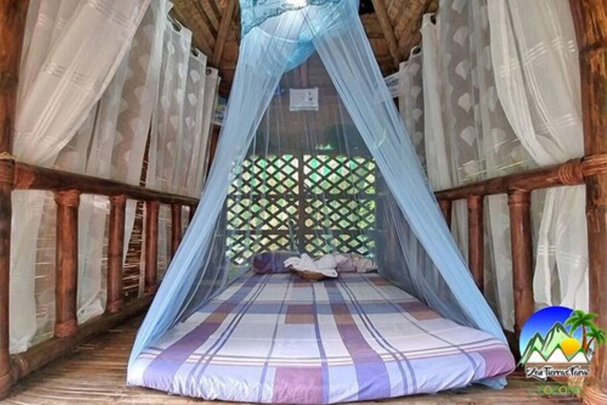 Une pièce avec un lit placé sous un dais bleu, des murs en bois et une fenêtre à croisillons.