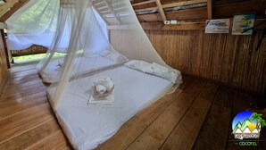 A wooden cabin with a bed under a mosquito net, a small table with a towel, and a wooden ceiling. - Zen Tierras Farm powered by Cocotel (Dingalan)