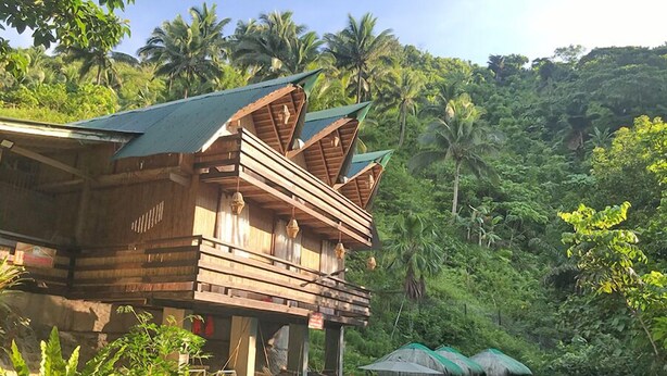 A wooden building with a sloped roof, surrounded by lush greenery and palm trees. - Zen Tierras Farm powered by Cocotel (Dingalan)