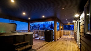 Et overdækket udeområde med jacuzzi, træterrasse og udsigt til bjerge.