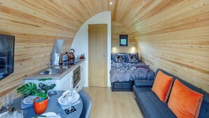 Uma cabana compacta e moderna, com cozinha compacta, área de refeições e espaço para dormir com sofá e almofadas.