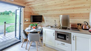 Cozinha compacta com forno embutido, micro-ondas e pia, teto de madeira e área de refeições com cadeiras e mesa.