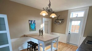 A kitchen with a wooden floor, white cabinetry, a dining table with two chairs, a stove, and a pendant light fixture.