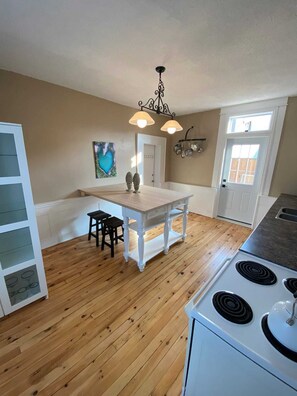 A kitchen with a wooden floor, white cabinetry, a dining table with two chairs, a stove, and a pendant light fixture.