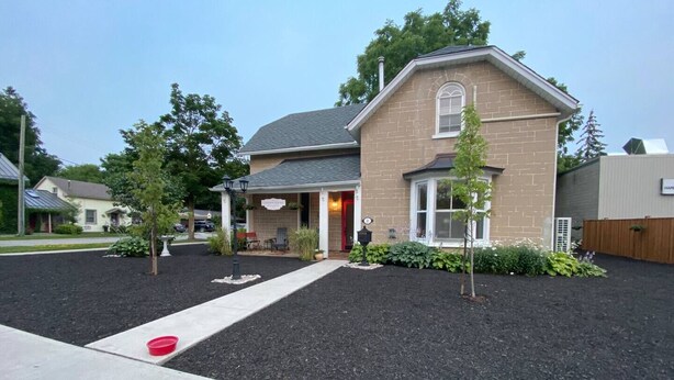 A two-story house with a brick exterior, a front porch with chairs, and a small garden area.