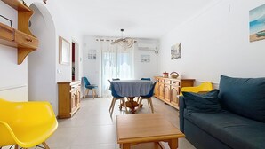 Una sala de estar con sofá, una mesa de comedor con sillas, una zona de cocina con armarios y un pasillo que conduce a otra habitación.