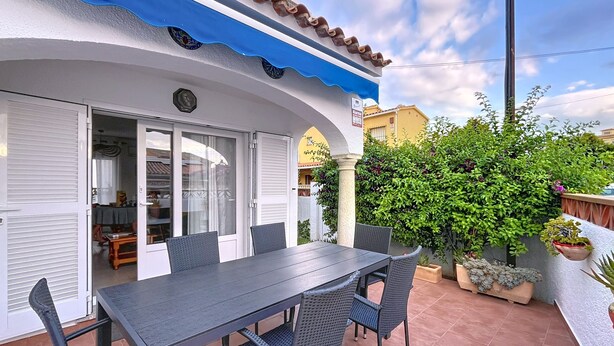 Un patio al aire libre con una mesa y sillas, un acceso cubierto y un jardín con diversas plantas.