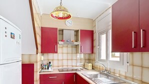 Una cocina con armarios rojos, un refrigerador blanco, un lavamanos y una ventana.