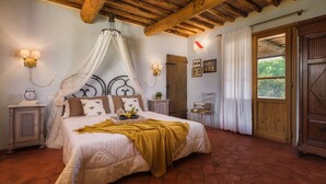 Un dormitorio con cama a dosel, vigas de madera, una puerta rústica y vistas por una ventana.