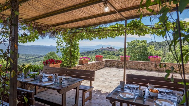 Un espace de restauration en plein air avec des murs en pierre, des bancs en bois et des tables prévues pour deux personnes.