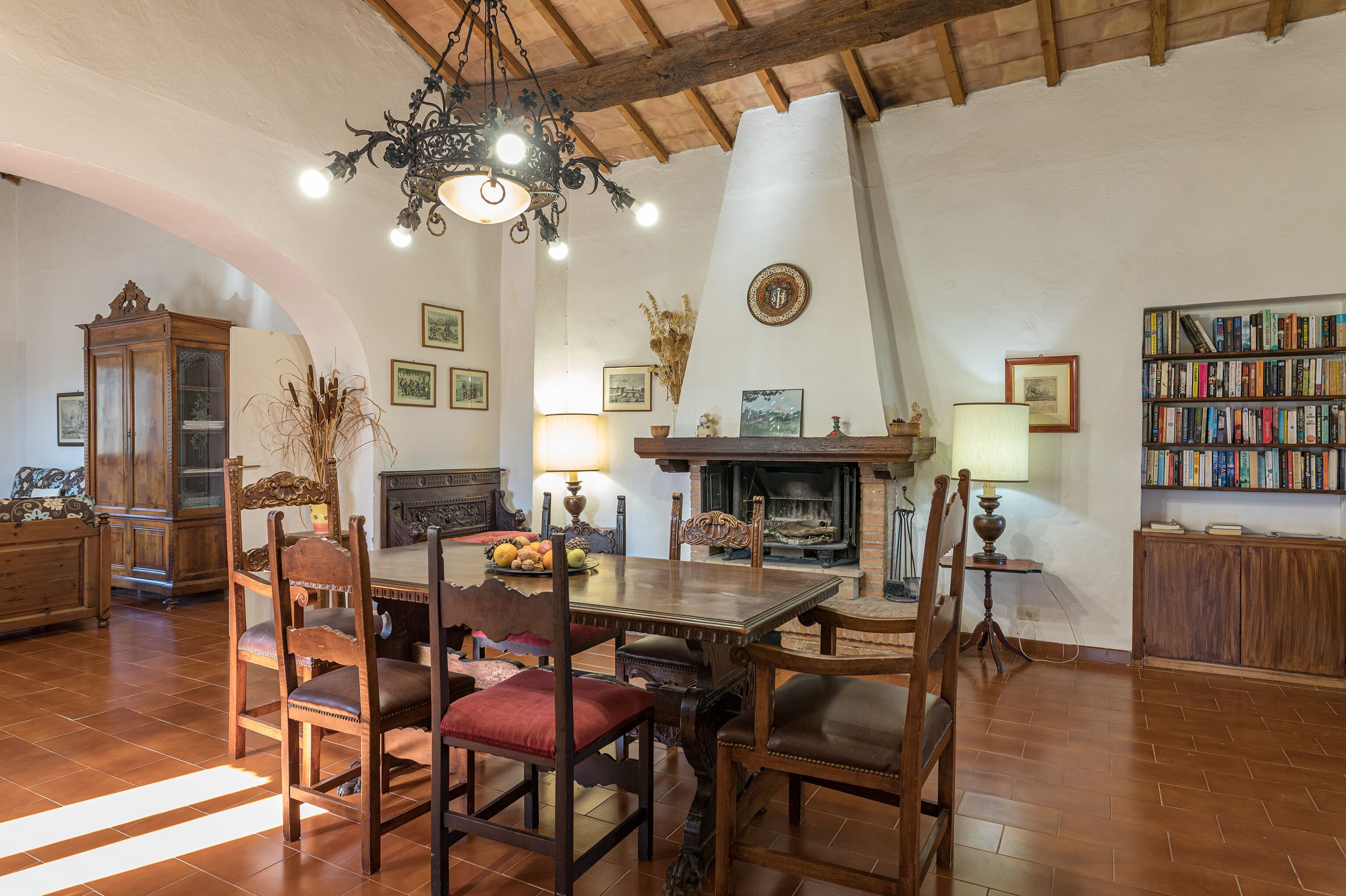 Un salon chaleureux avec une table à manger en bois, des chaises, une cheminée, des étagères et un lustre.
