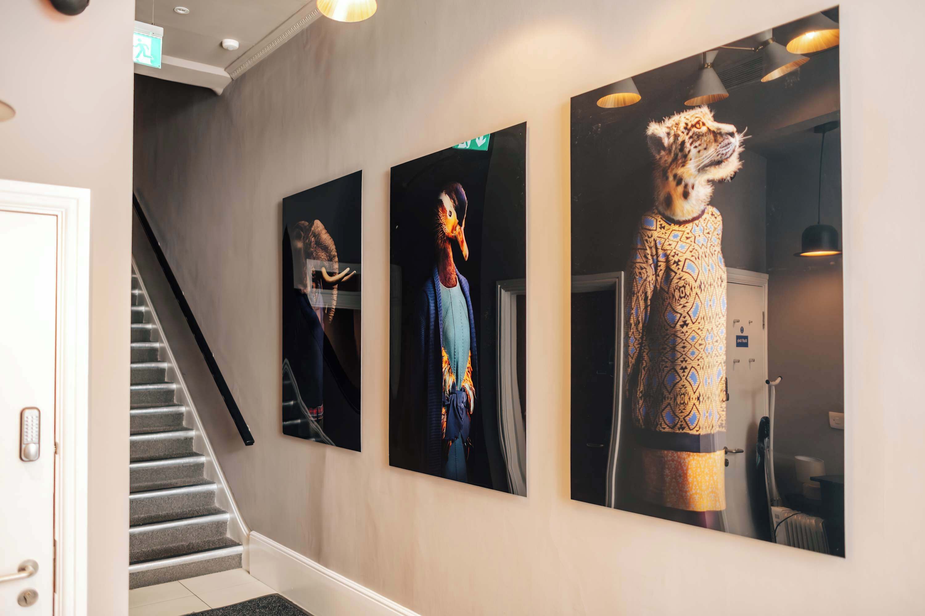 A hallway with a staircase, three framed artworks on the wall, and a door.
